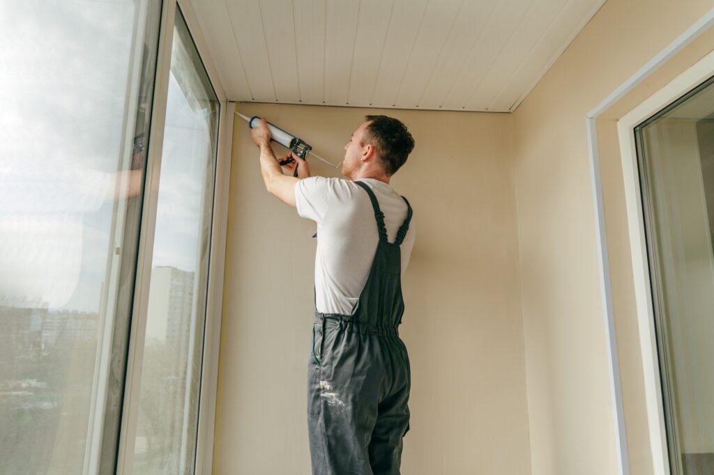 Young man wearing overalls sealing cracks between window and tri